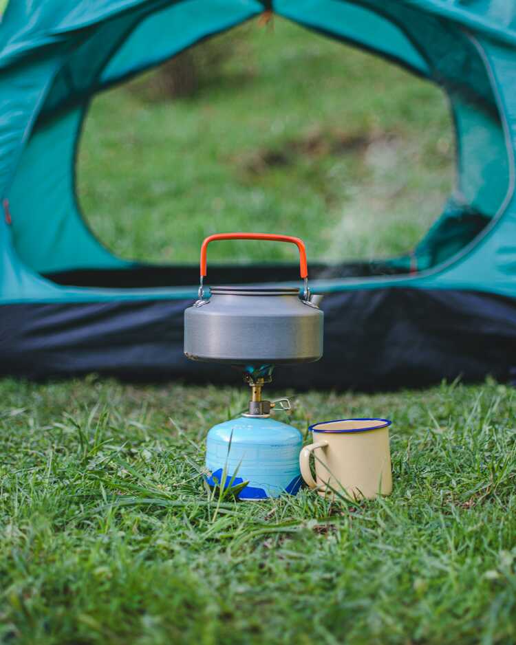 Tent met daarvoor fluitketel op camping gasbrander. Bron Unsplash Foto Alireza Shojaei.